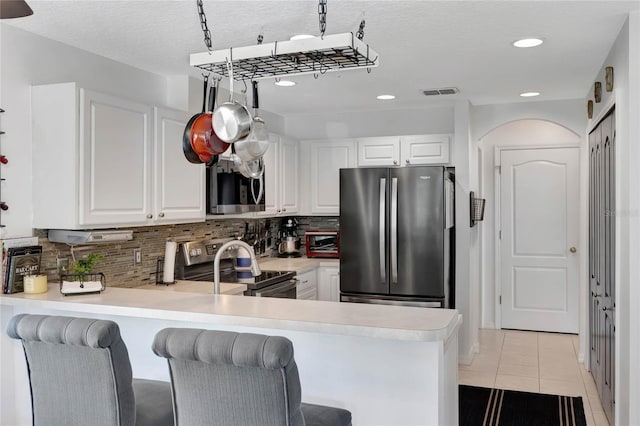 kitchen featuring appliances with stainless steel finishes, white cabinets, backsplash, light tile patterned floors, and kitchen peninsula