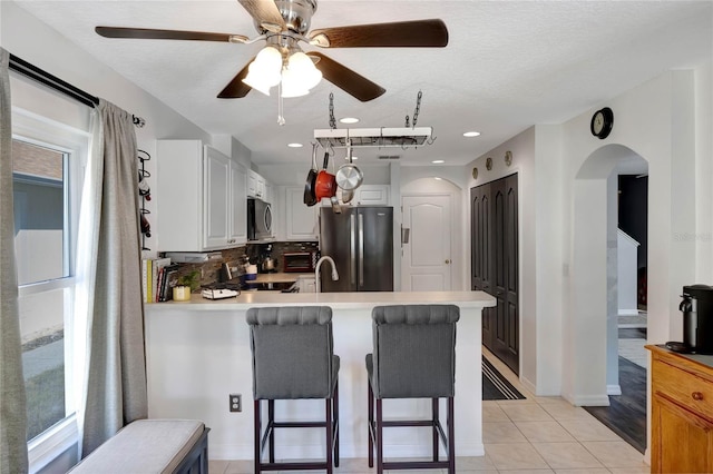 kitchen featuring light tile patterned floors, stainless steel appliances, white cabinets, a kitchen bar, and kitchen peninsula