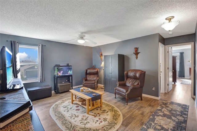 living room with ceiling fan, light hardwood / wood-style flooring, and a textured ceiling