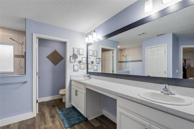 bathroom featuring a tile shower, hardwood / wood-style flooring, vanity, toilet, and a textured ceiling