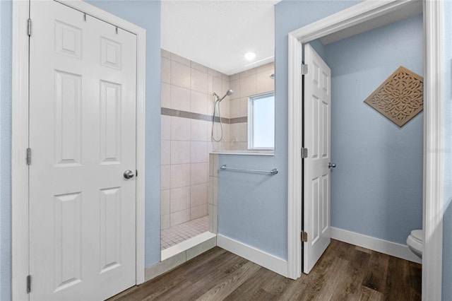 bathroom featuring hardwood / wood-style floors, a tile shower, and toilet