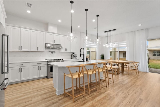 kitchen with decorative light fixtures, a center island with sink, white cabinetry, and stainless steel appliances