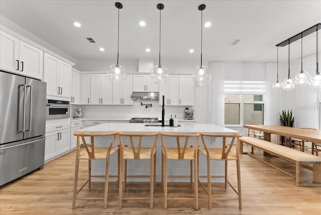 kitchen with white cabinets, stainless steel appliances, a center island with sink, and decorative light fixtures