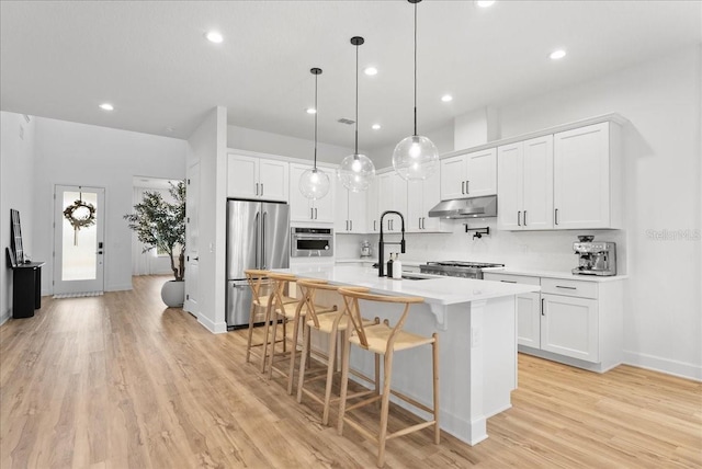 kitchen featuring decorative light fixtures, a center island with sink, white cabinetry, and stainless steel appliances