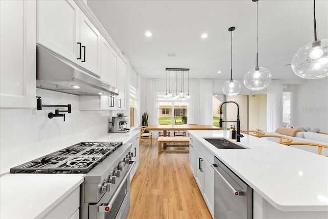 kitchen with appliances with stainless steel finishes, decorative light fixtures, white cabinetry, an island with sink, and sink