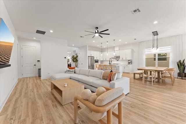 living room with ceiling fan, sink, and light wood-type flooring