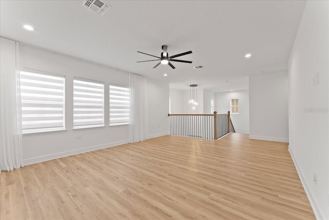 empty room with ceiling fan with notable chandelier and light hardwood / wood-style floors