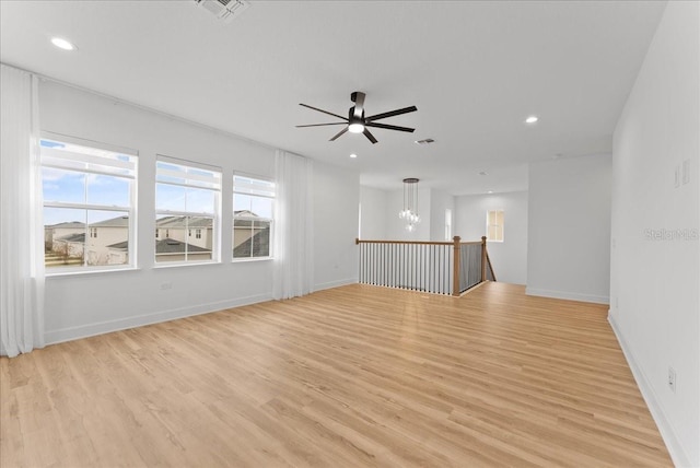 spare room with ceiling fan with notable chandelier and light hardwood / wood-style flooring