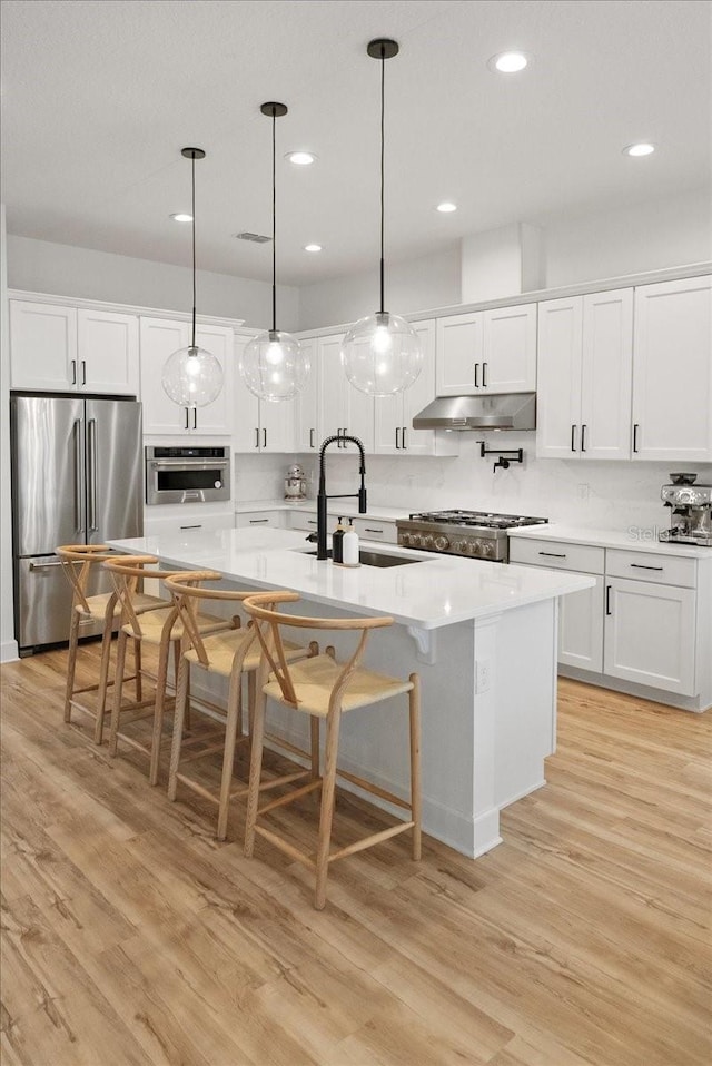 kitchen with pendant lighting, appliances with stainless steel finishes, white cabinetry, sink, and a center island with sink