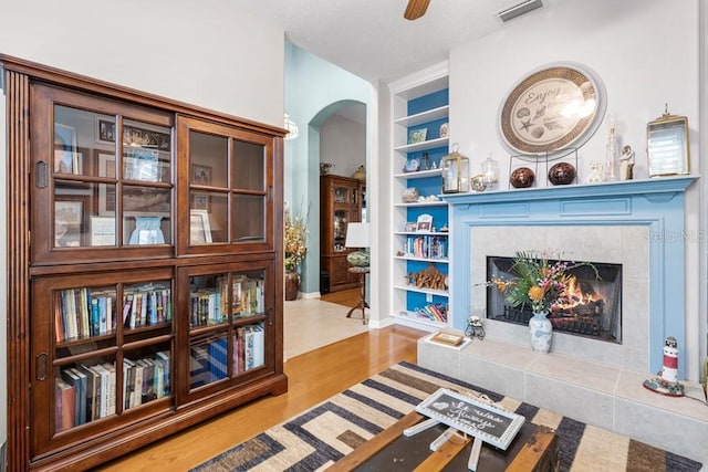 sitting room with built in shelves, ceiling fan, a fireplace, and light hardwood / wood-style flooring