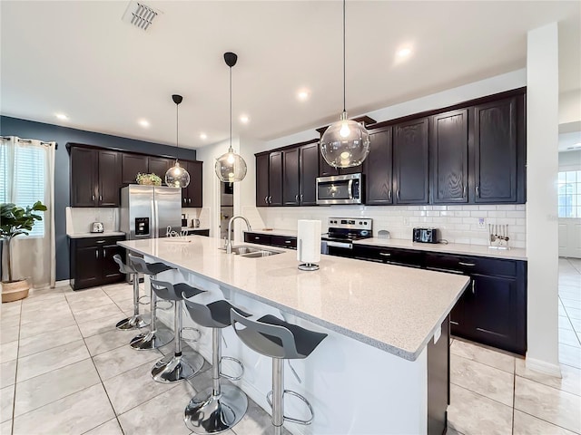 kitchen featuring sink, decorative light fixtures, light tile patterned floors, a center island with sink, and stainless steel appliances