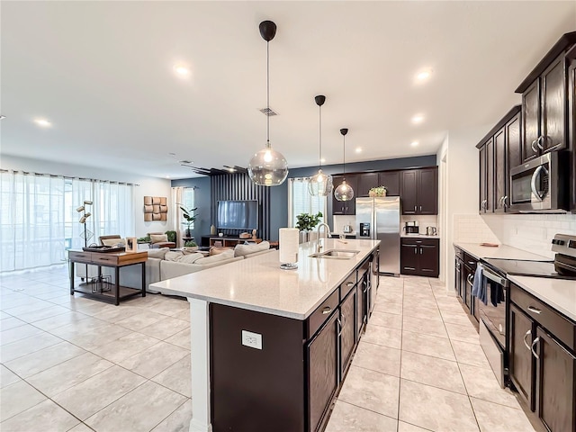 kitchen with pendant lighting, stainless steel appliances, an island with sink, light tile patterned floors, and dark brown cabinets