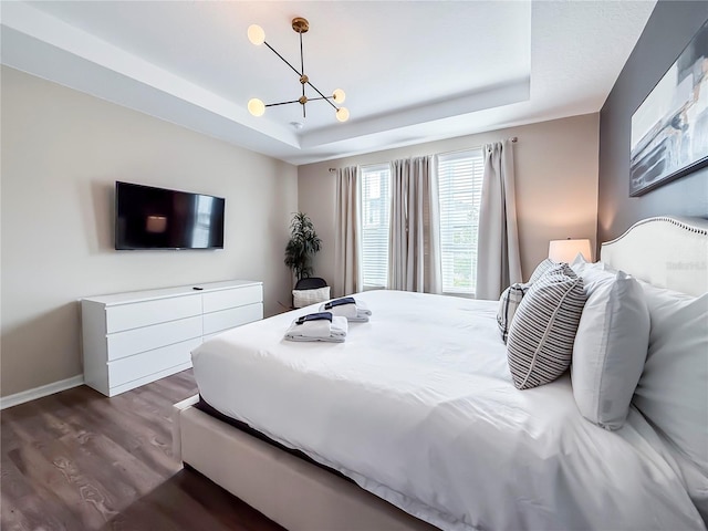 bedroom with dark wood-type flooring, a tray ceiling, and a notable chandelier