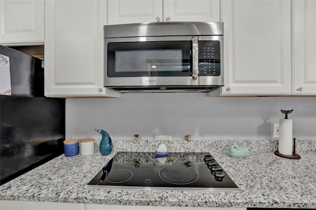 kitchen with white cabinets, black electric stovetop, and light stone counters