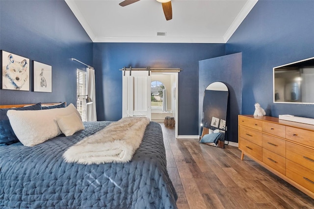 bedroom featuring ornamental molding, dark hardwood / wood-style floors, ceiling fan, and a barn door