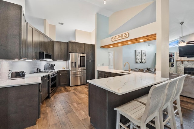 kitchen with kitchen peninsula, appliances with stainless steel finishes, hardwood / wood-style flooring, decorative backsplash, and a breakfast bar area