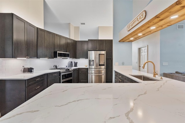 kitchen featuring light stone countertops, sink, dark brown cabinets, backsplash, and stainless steel appliances