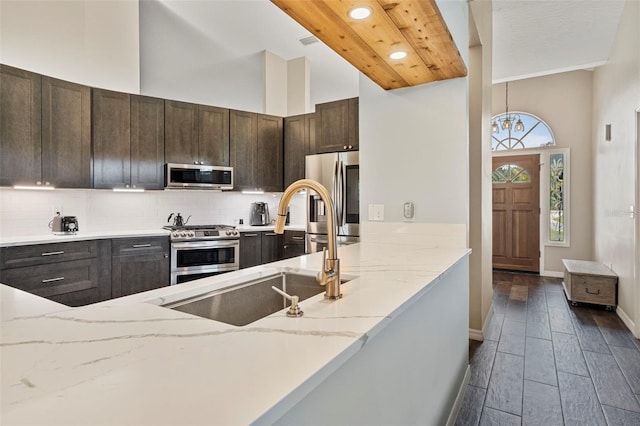 kitchen featuring a high ceiling, light stone countertops, appliances with stainless steel finishes, sink, and dark brown cabinets