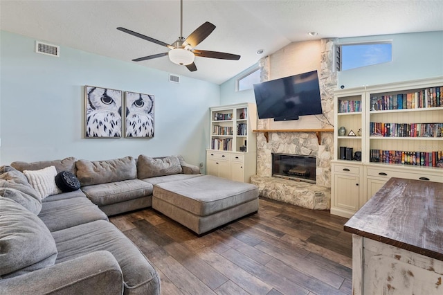 living room with a healthy amount of sunlight, vaulted ceiling, a stone fireplace, and dark hardwood / wood-style flooring