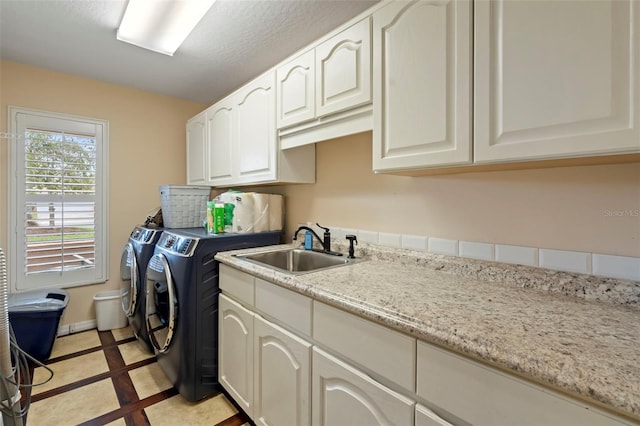 clothes washing area featuring light tile patterned floors, cabinets, washer and clothes dryer, and sink