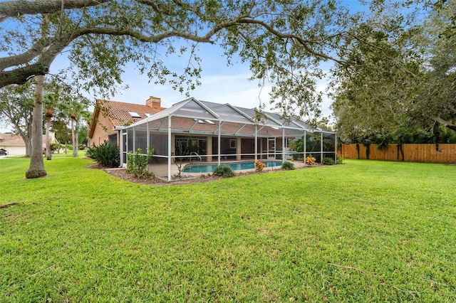 rear view of property featuring glass enclosure, a fenced in pool, and a lawn