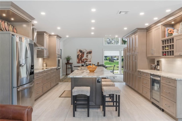 kitchen featuring appliances with stainless steel finishes, a breakfast bar area, beverage cooler, light stone counters, and a spacious island