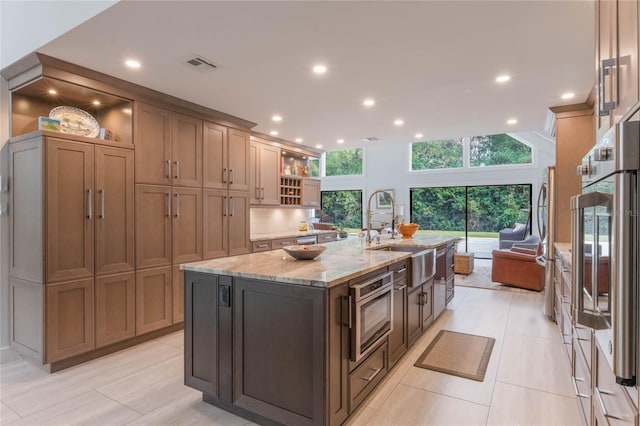 kitchen featuring sink, refrigerator, light stone counters, oven, and a large island with sink