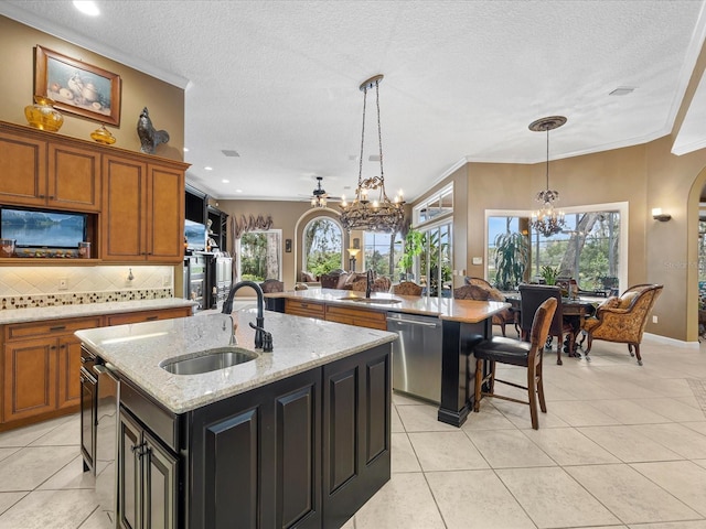 kitchen featuring pendant lighting, sink, stainless steel dishwasher, light stone countertops, and a center island with sink