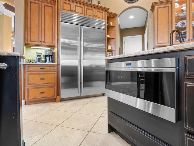 kitchen featuring backsplash, oven, stainless steel built in fridge, and light tile patterned floors