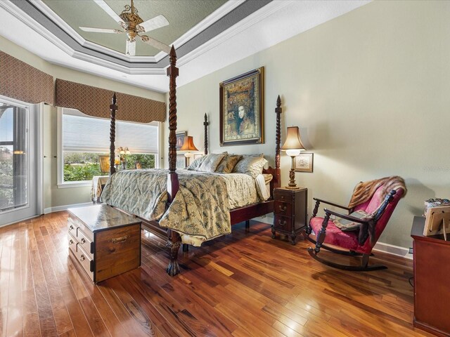 bedroom with dark hardwood / wood-style flooring, access to outside, ceiling fan, a tray ceiling, and crown molding