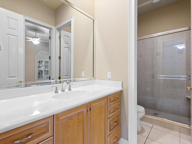 bathroom with tile patterned floors, toilet, vanity, a shower with door, and ceiling fan