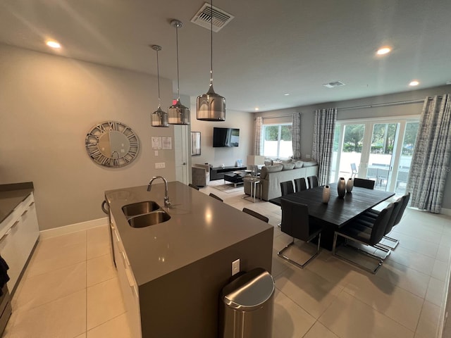 kitchen with sink, decorative light fixtures, white cabinetry, light tile patterned floors, and an island with sink