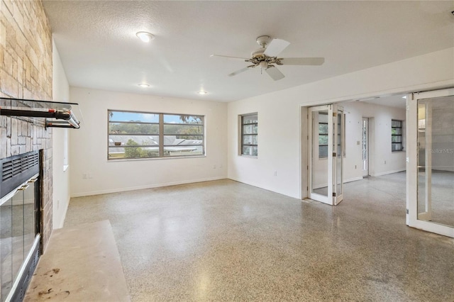 unfurnished living room with ceiling fan, a stone fireplace, french doors, and a textured ceiling