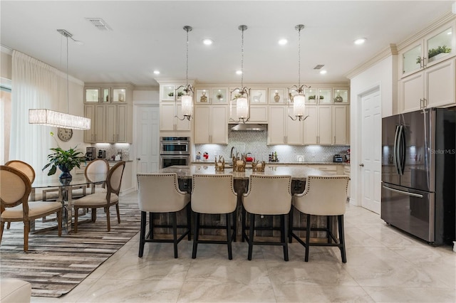 kitchen featuring pendant lighting, crown molding, stainless steel appliances, tasteful backsplash, and an island with sink