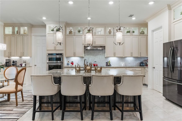 kitchen with black fridge, double oven, an island with sink, and decorative backsplash