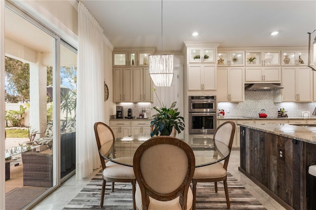 kitchen with cream cabinets, light stone countertops, double oven, and hanging light fixtures