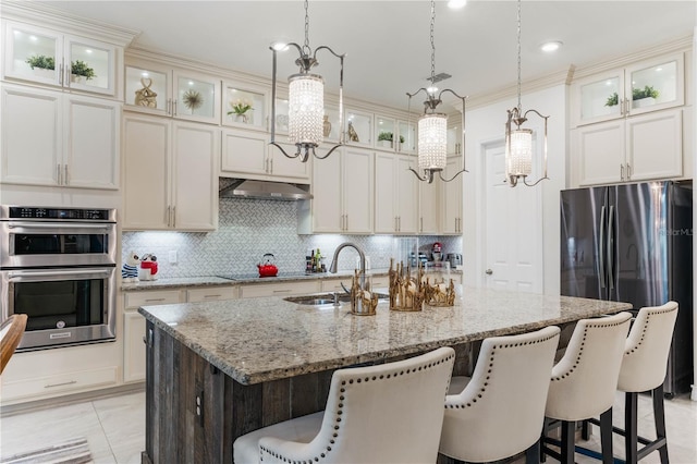 kitchen featuring light tile patterned floors, appliances with stainless steel finishes, light stone counters, extractor fan, and a center island with sink