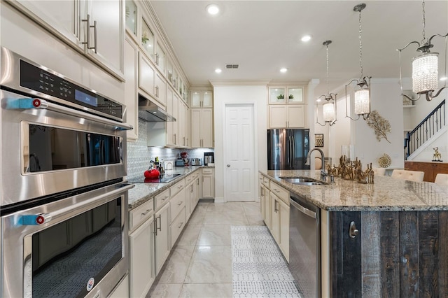 kitchen featuring sink, hanging light fixtures, black appliances, a center island with sink, and decorative backsplash