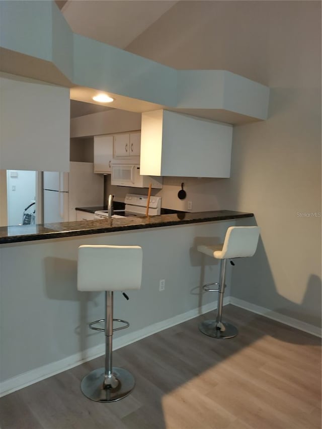 kitchen with white cabinetry, white appliances, a breakfast bar area, and wood-type flooring