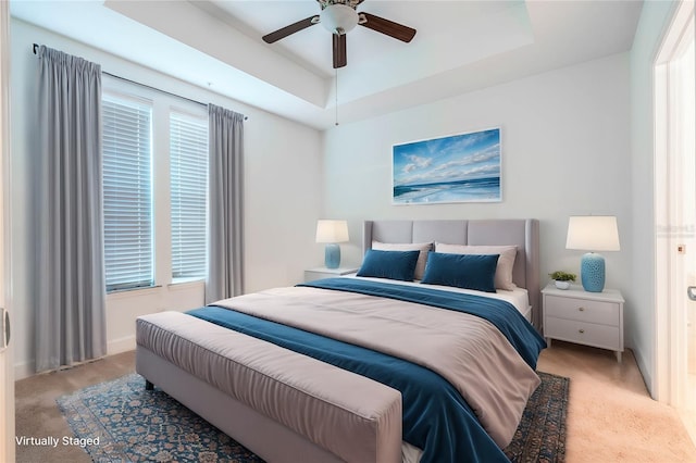 carpeted bedroom with ceiling fan and a tray ceiling