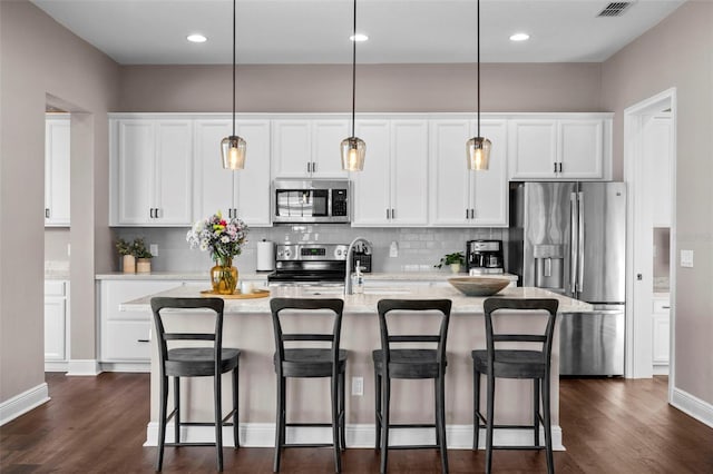 kitchen with pendant lighting, appliances with stainless steel finishes, white cabinets, a kitchen island with sink, and a breakfast bar area