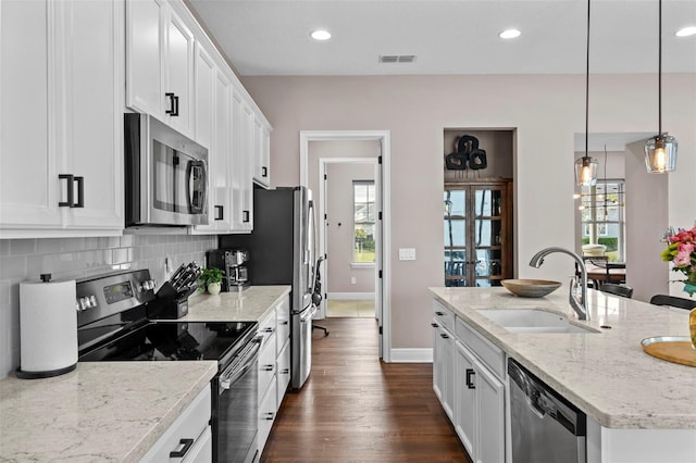 kitchen with white cabinets, decorative light fixtures, stainless steel appliances, an island with sink, and sink