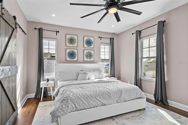 bedroom featuring ceiling fan, dark hardwood / wood-style flooring, and a barn door