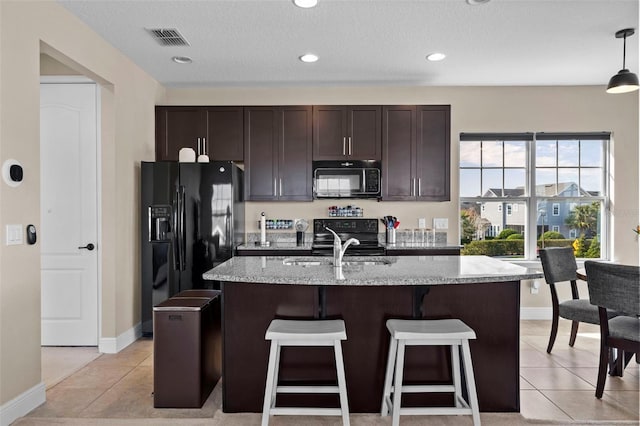 kitchen featuring light tile patterned floors, black appliances, and an island with sink