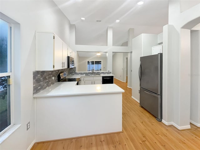 kitchen with appliances with stainless steel finishes, tasteful backsplash, sink, white cabinets, and kitchen peninsula