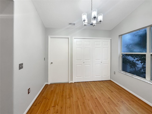 unfurnished bedroom with wood-type flooring, a textured ceiling, an inviting chandelier, and a closet