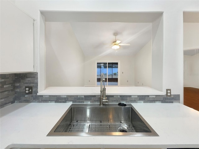 kitchen with white cabinetry, lofted ceiling, sink, backsplash, and ceiling fan