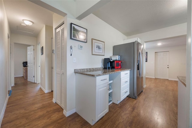 kitchen with dark wood-type flooring, stainless steel fridge, light stone counters, and white cabinets