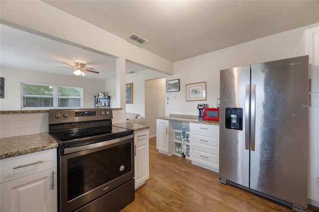 kitchen with appliances with stainless steel finishes, tasteful backsplash, white cabinets, light stone counters, and light hardwood / wood-style floors