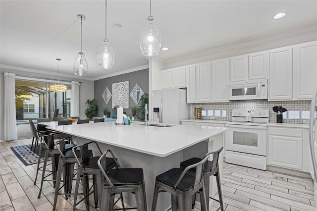 kitchen with a large island with sink, a kitchen breakfast bar, white cabinets, and white appliances